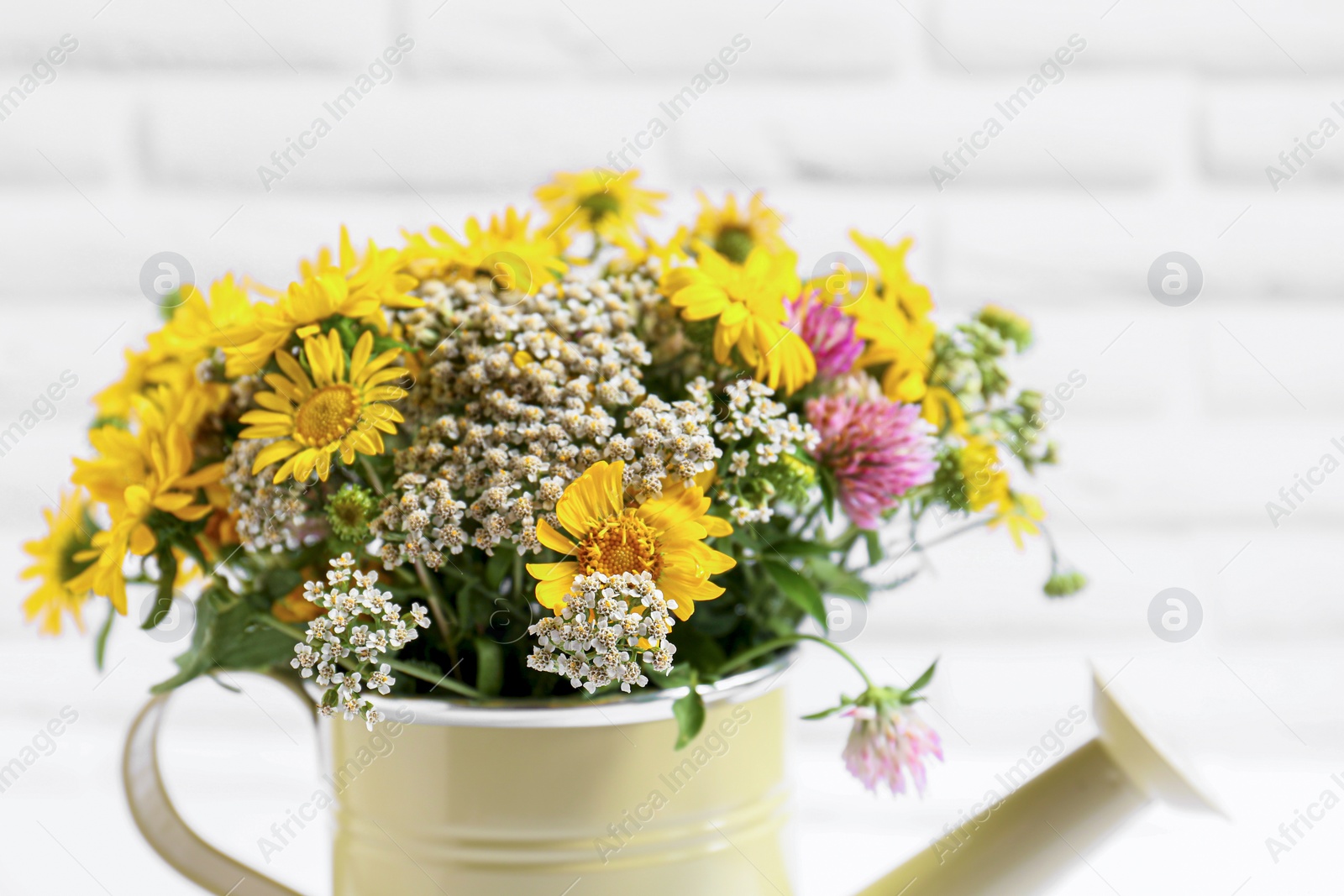 Photo of Beautiful bouquet of bright wildflowers in watering can near white brick wall, closeup