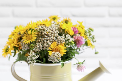 Beautiful bouquet of bright wildflowers in watering can near white brick wall, closeup