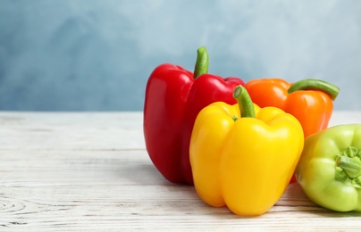 Photo of Ripe bell peppers on white wooden table against light blue background, space for text