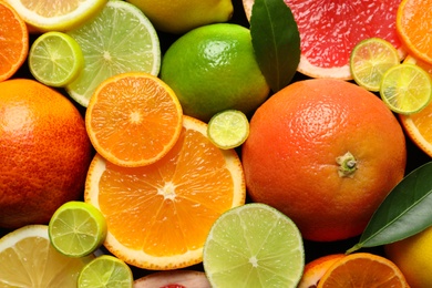 Photo of Sliced and whole citrus fruits with leaves as background, top view