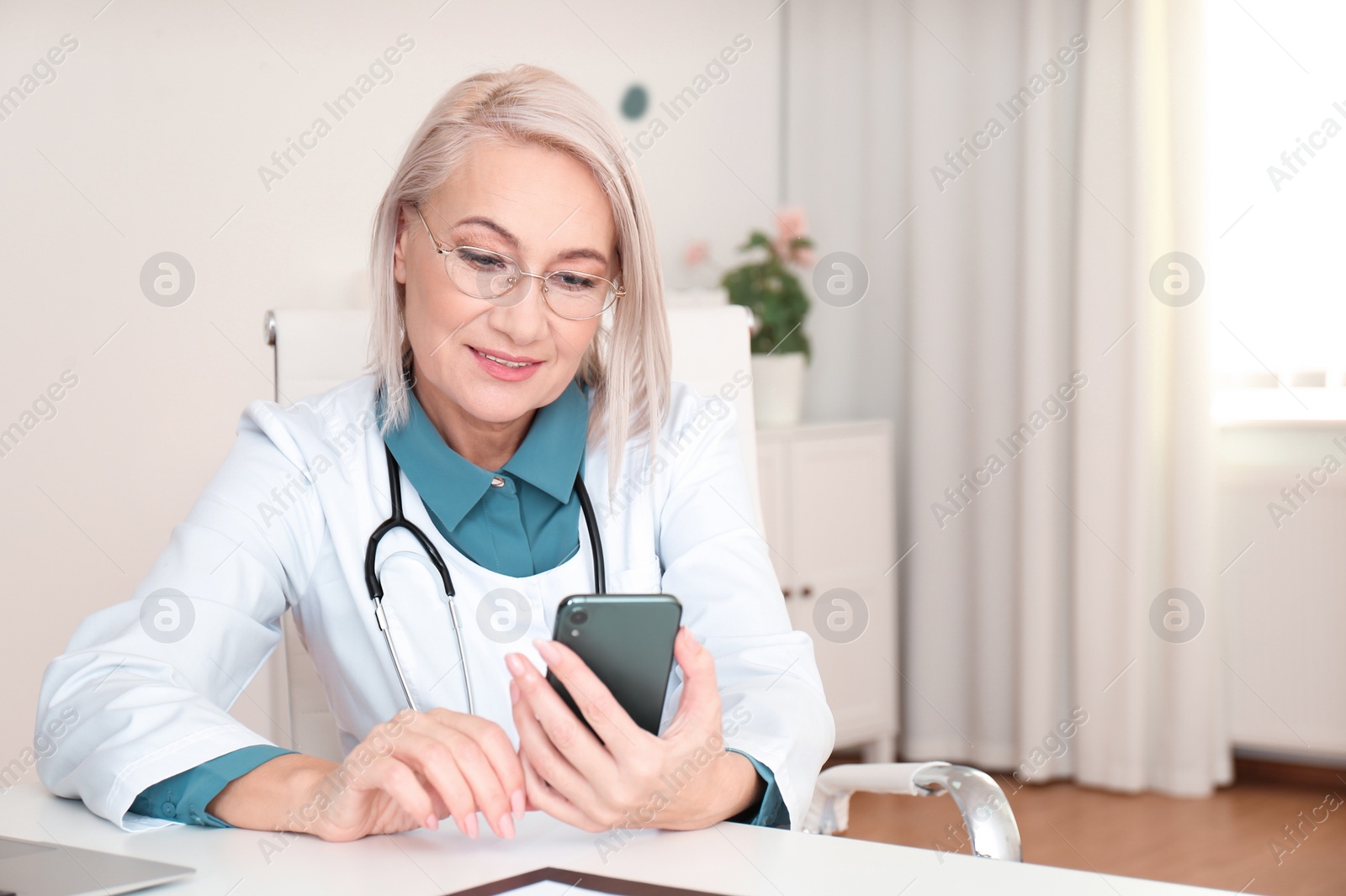 Photo of Mature female doctor with smartphone at table in office