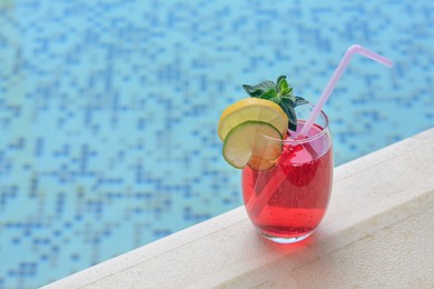 Glass of delicious cocktail near swimming pool, space for text. Refreshing drink