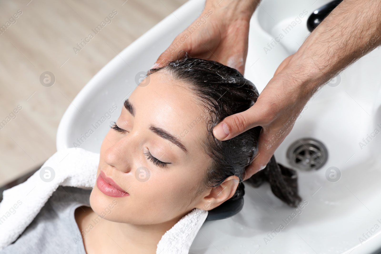 Photo of Stylist washing client's hair at sink in beauty salon