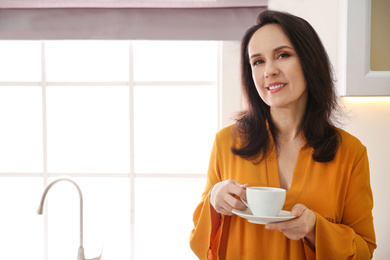 Photo of Beautiful mature woman with cup of coffee at home. Space for text