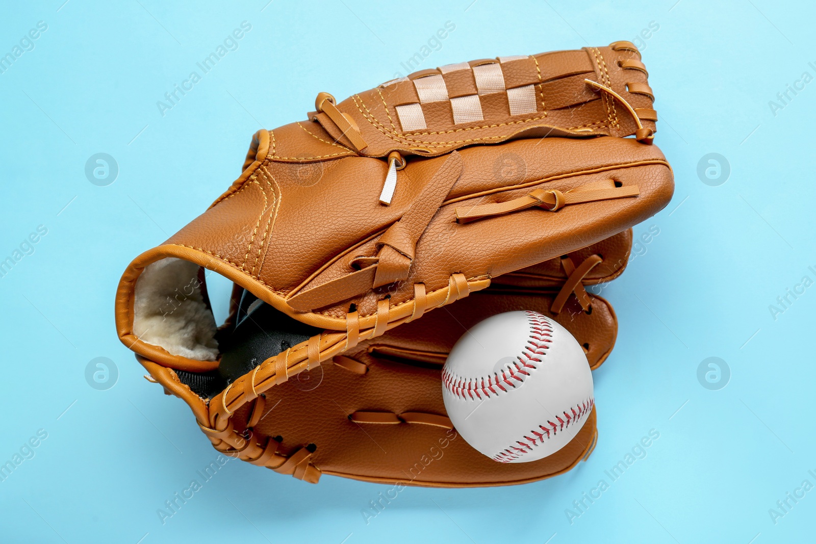 Photo of Catcher's mitt and baseball ball on light blue background, top view. Sports game
