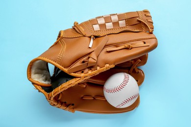Photo of Catcher's mitt and baseball ball on light blue background, top view. Sports game