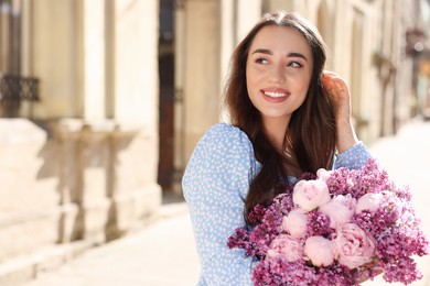 Photo of Beautiful woman with bouquet of spring flowers on city street, space for text