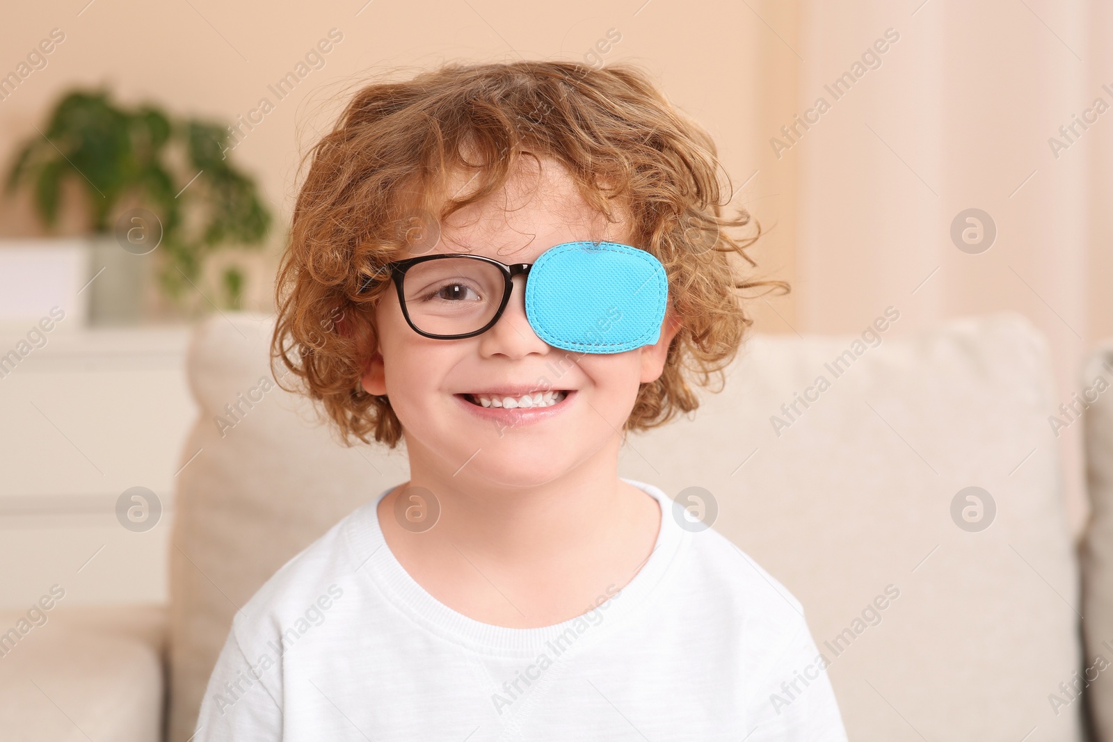 Photo of Happy boy with eye patch on glasses indoors. Strabismus treatment