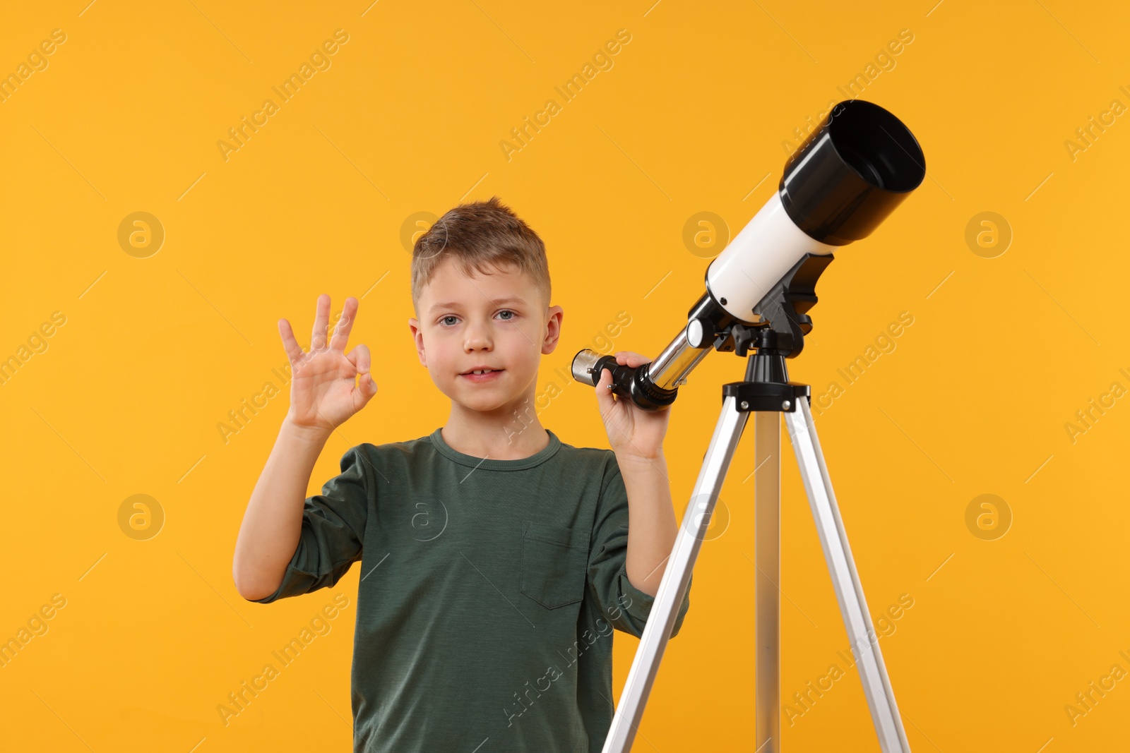 Photo of Cute little boy with telescope showing ok gesture on orange background