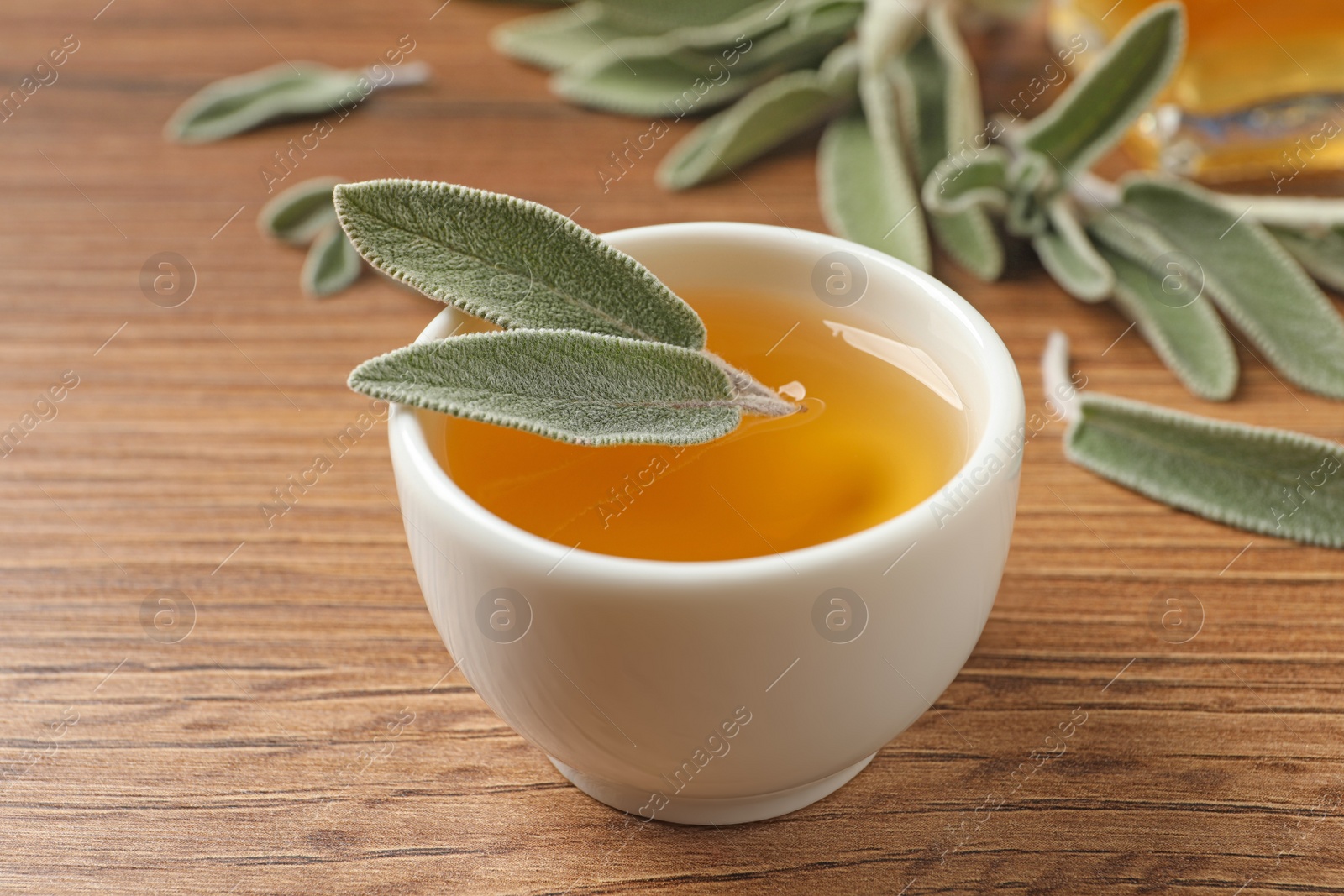 Photo of Bowl of essential sage oil and leaves on wooden table