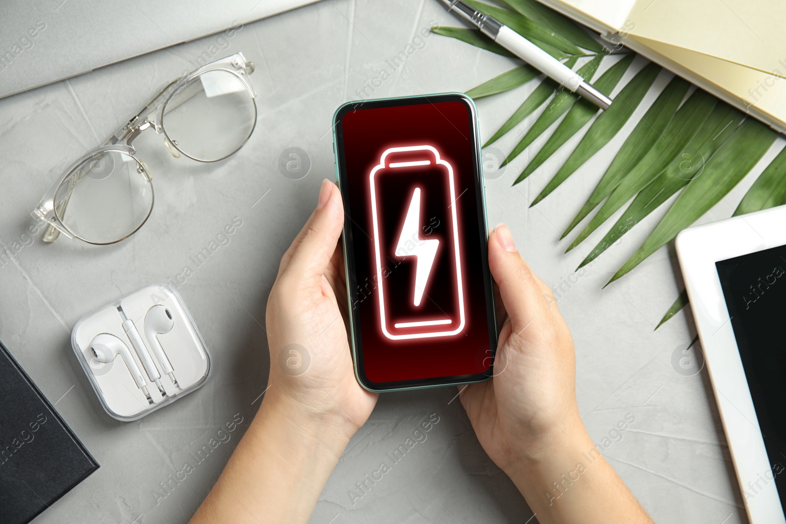 Image of Young woman holding smartphone with low battery at grey table, top view