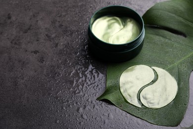 Photo of Package of under eye patches and tropical leaf on grey background, space for text. Cosmetic product