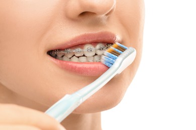 Photo of Woman with dental braces cleaning teeth on white background, closeup