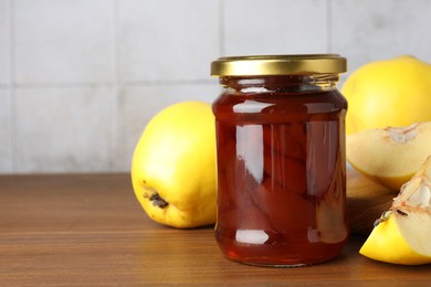 Photo of Tasty homemade quince jam in jar and fruits on wooden table, closeup. Space for text