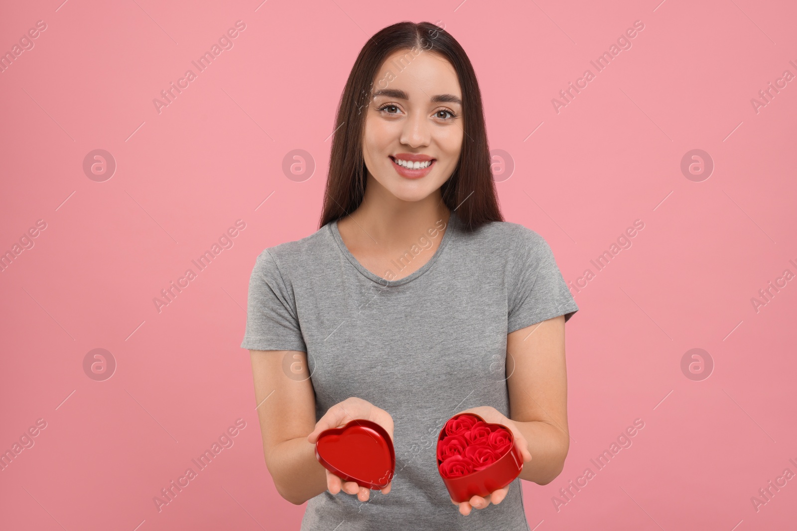 Photo of Happy young woman holding red heart shaped gift box on pink background