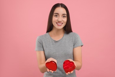 Happy young woman holding red heart shaped gift box on pink background