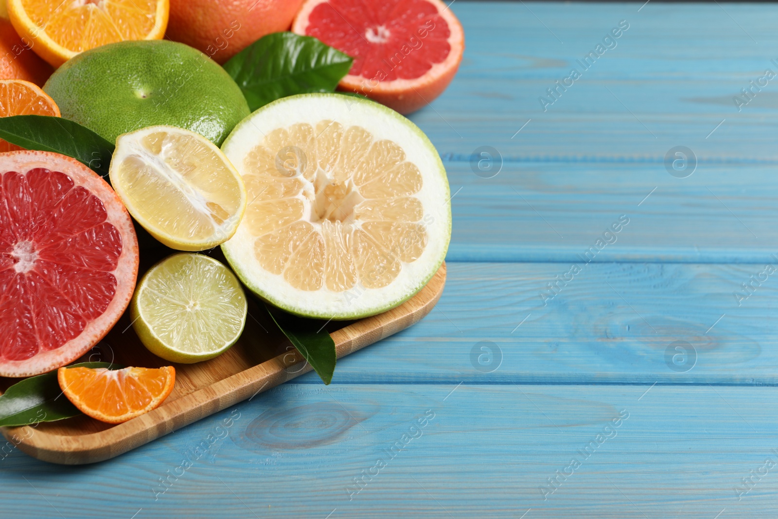 Photo of Different citrus fruits with fresh leaves on light blue wooden table. Space for text