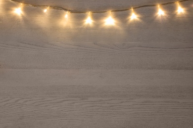 Photo of Beautiful glowing Christmas lights on white wooden table, top view. Space for text