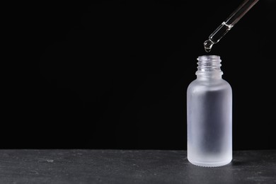 Photo of Dripping cosmetic serum from pipette into bottle on grey table, space for text