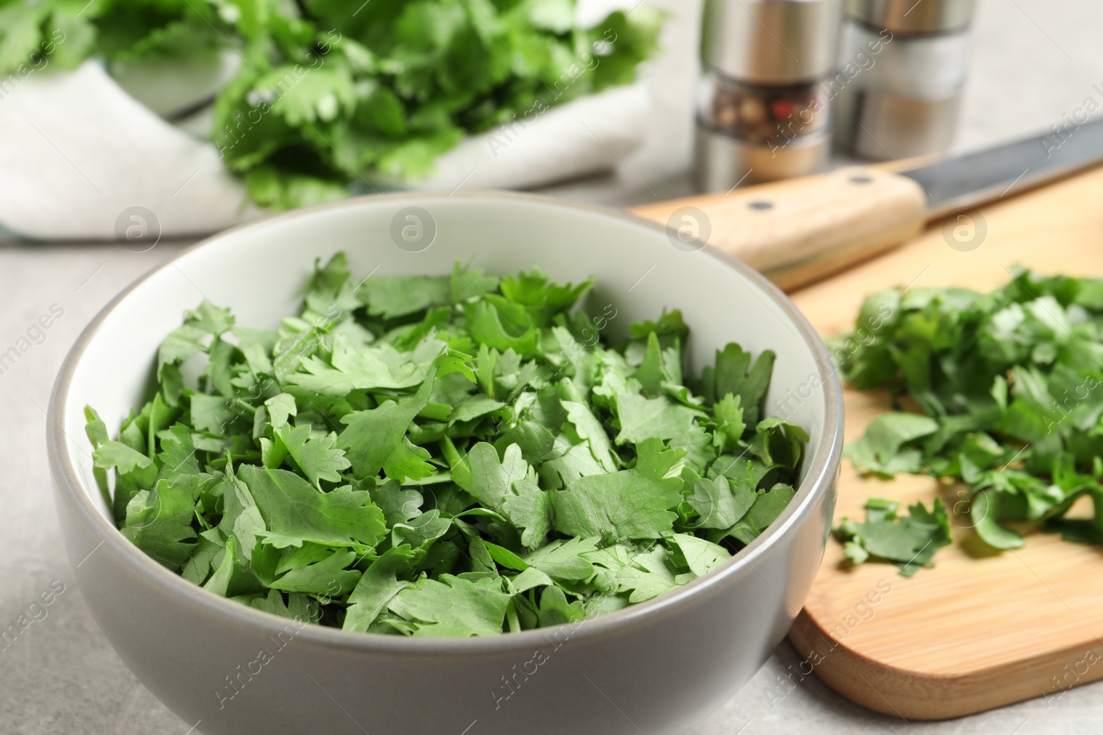 Photo of Cut fresh green cilantro in bowl on light grey table, closeup