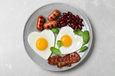 Plate of tasty breakfast with heart shaped fried eggs  on grey table, top view