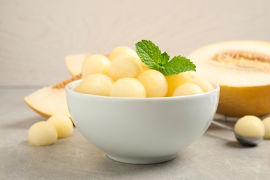 Photo of Melon balls and mint in bowl on light grey table, closeup