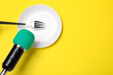 Photo of Making ASMR sounds with microphone, plate and fork on yellow background, flat lay. Space for text