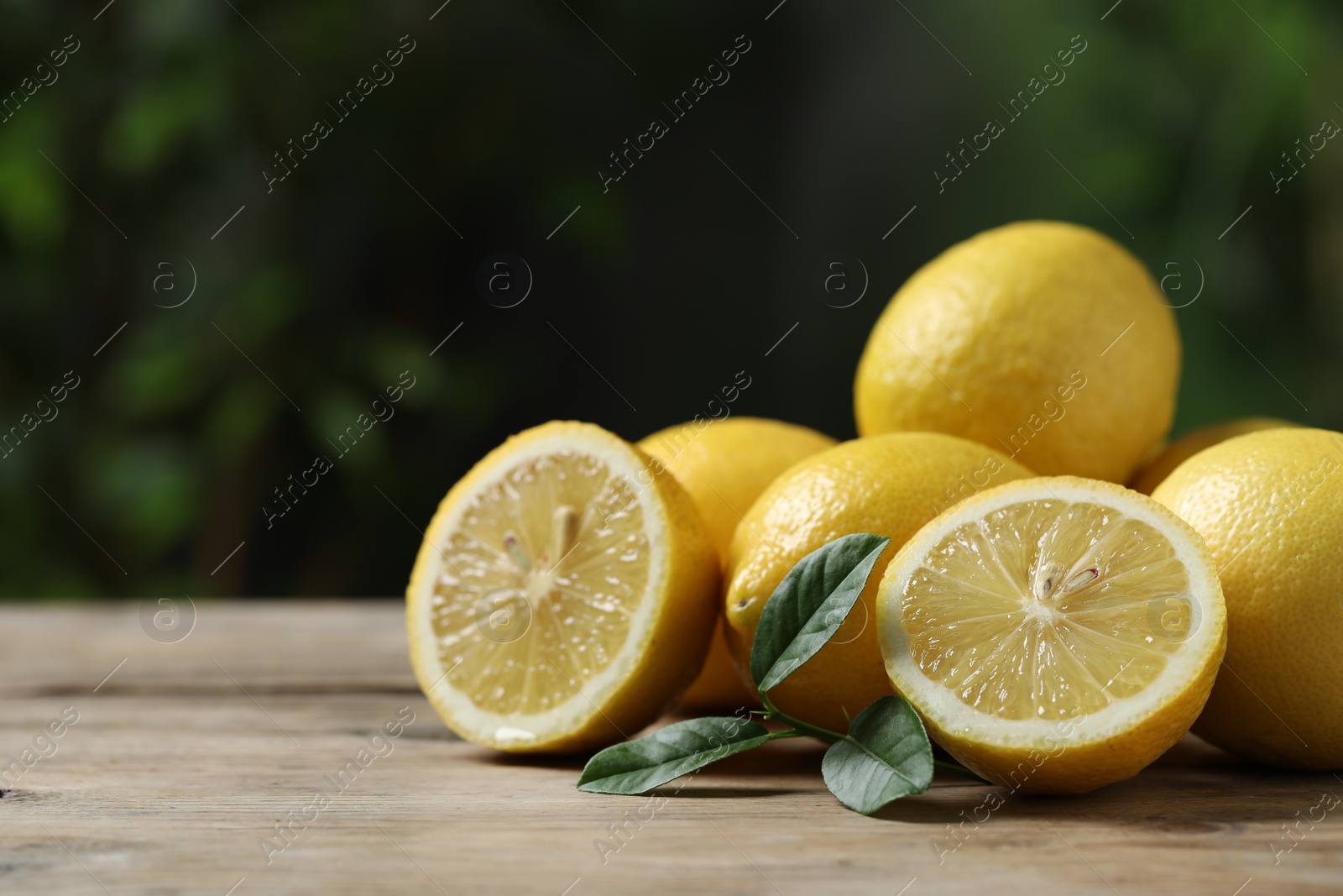 Photo of Fresh lemons and green leaves on wooden table, closeup. Space for text