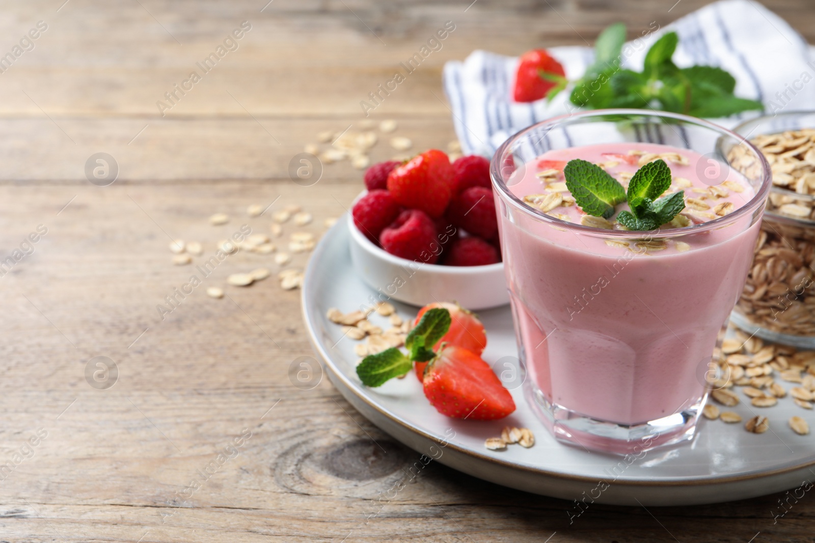 Photo of Glass of tasty berry smoothie with oatmeal on wooden table. Space for text