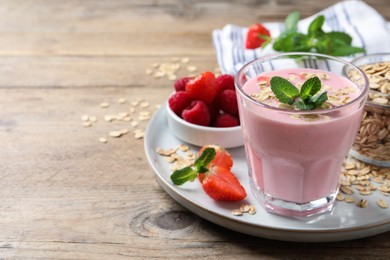 Photo of Glass of tasty berry smoothie with oatmeal on wooden table. Space for text