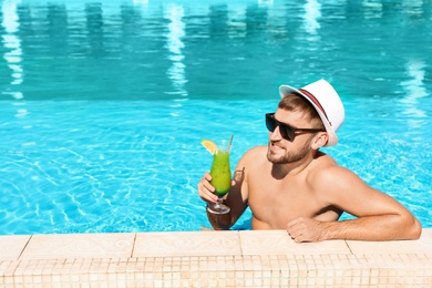 Young bearded man with refreshing cocktail in swimming pool at resort. Space for text