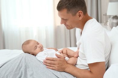 Happy father holding his cute sleeping baby on bed at home