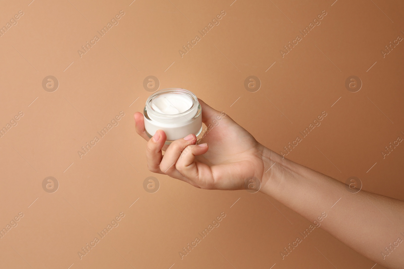 Photo of Woman holding jar of face cream on beige background, closeup. Space for text