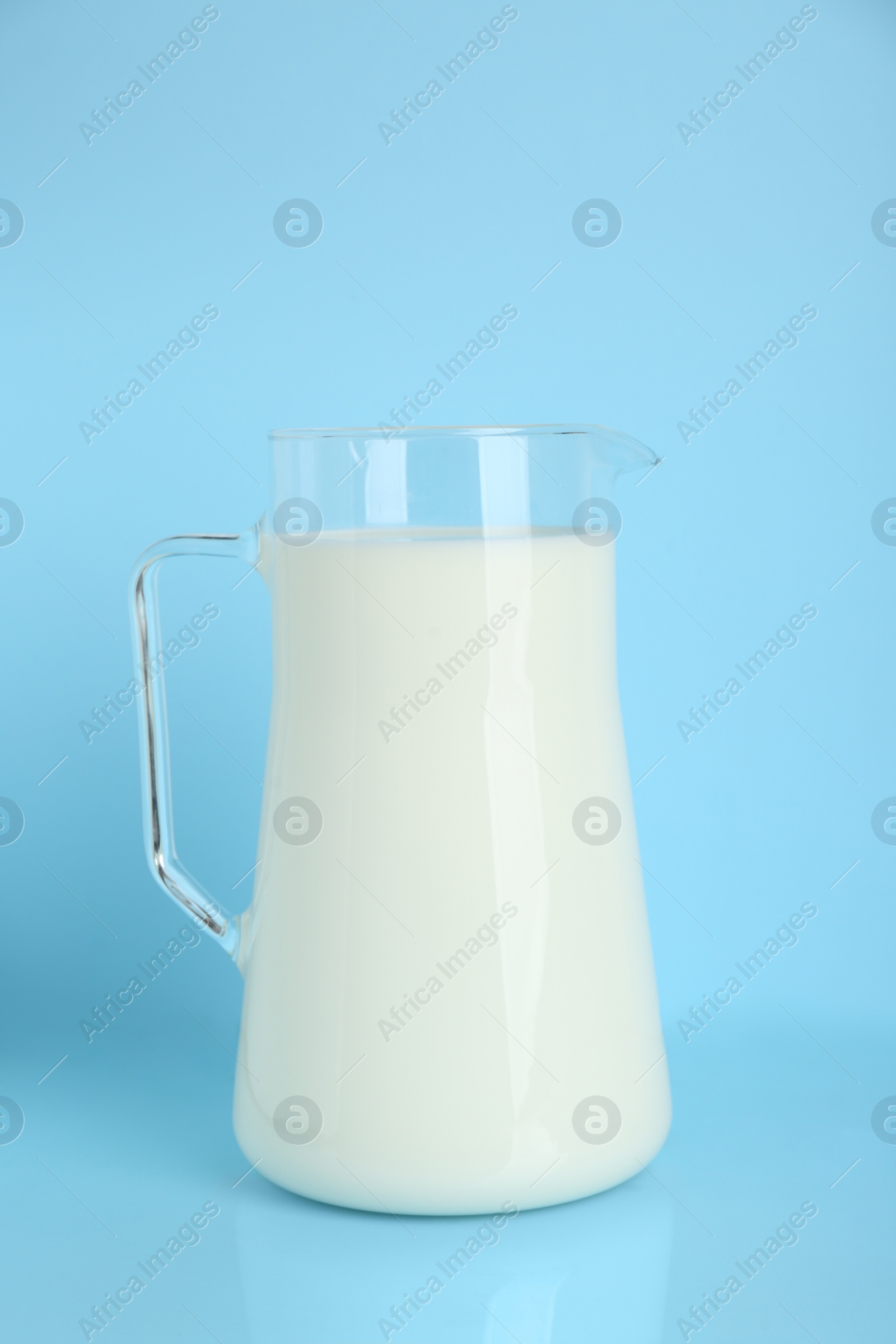 Photo of Jug of fresh milk on light blue background