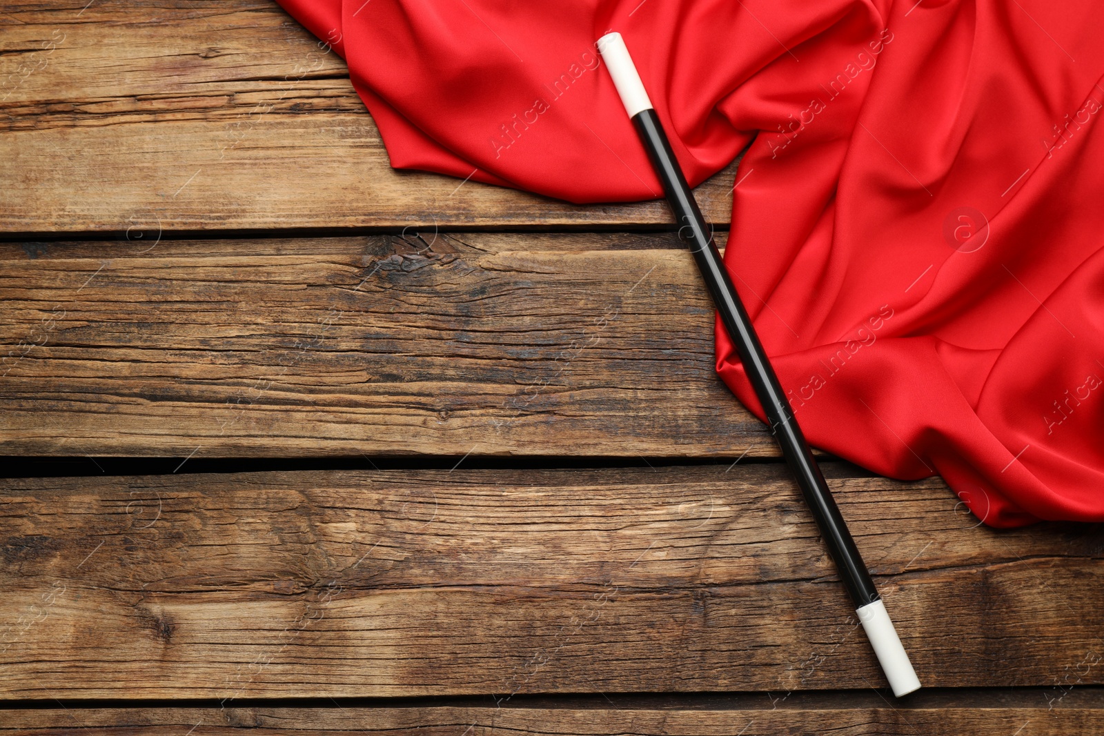 Photo of Beautiful black magic wand and red fabric on wooden table, top view. Space for text