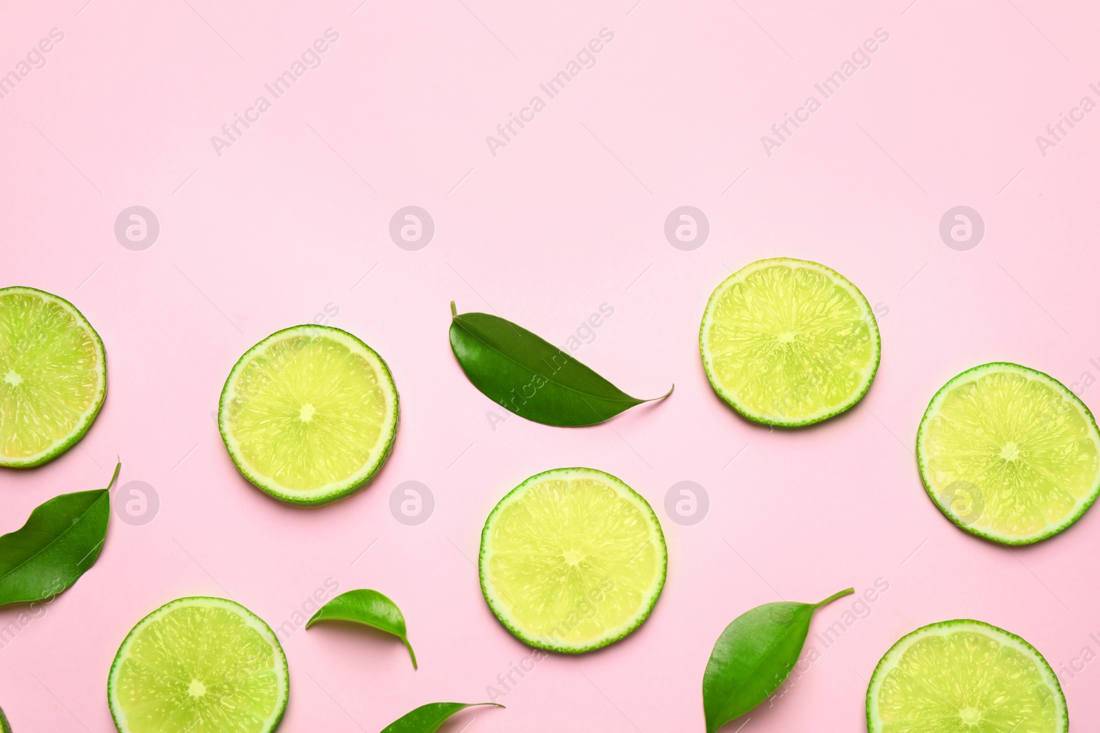 Photo of Juicy fresh lime slices and green leaves on pink background, flat lay. Space for text