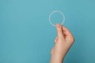Woman holding diaphragm vaginal contraceptive ring on light blue background, closeup. Space for text