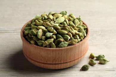 Bowl of dry cardamom pods on white wooden table, closeup