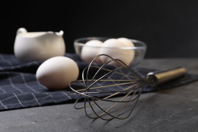 Metal whisk and raw eggs on dark grey table, closeup