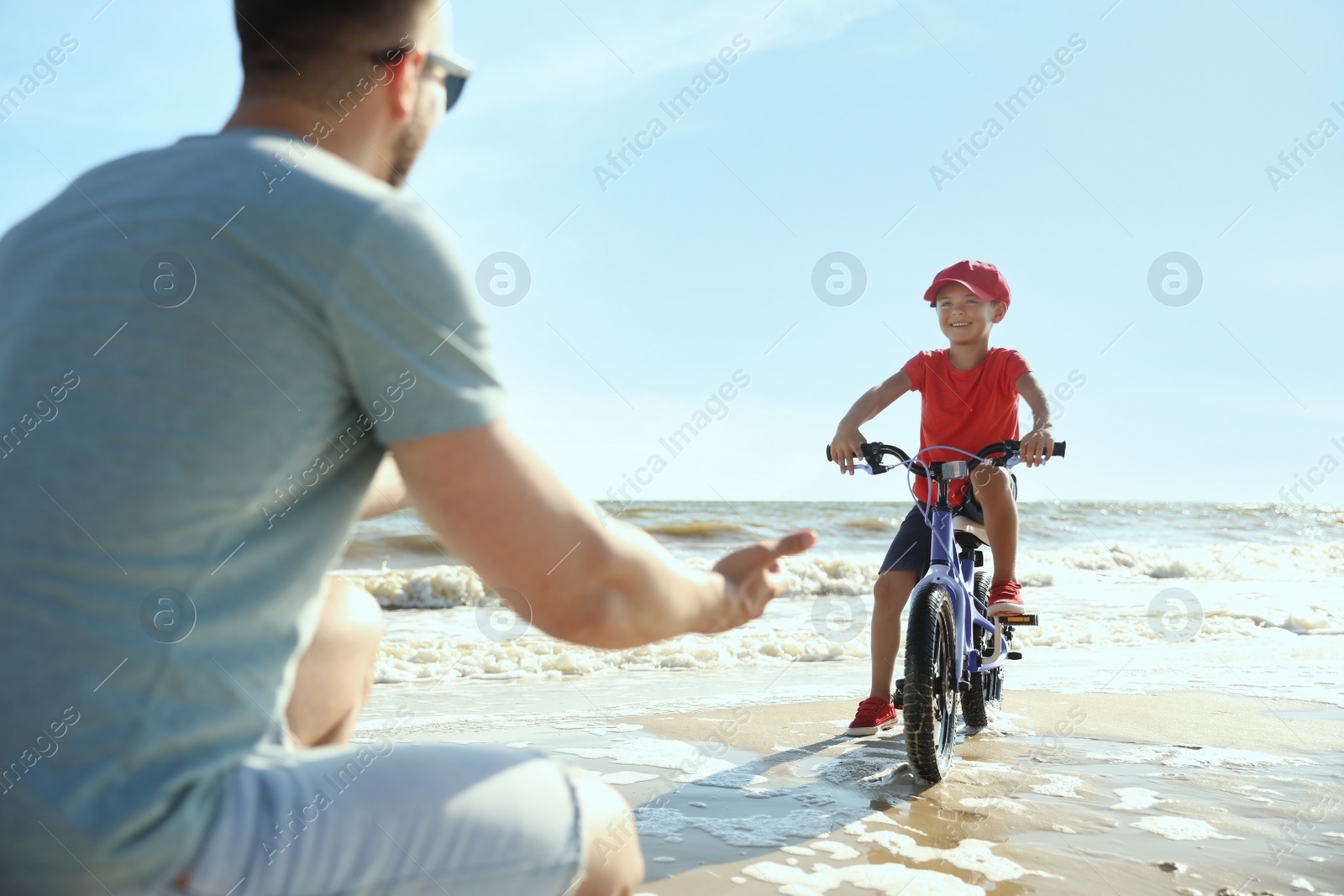 Photo of Happy father teaching son to ride bicycle on sandy beach near sea