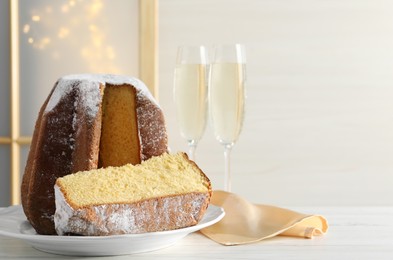 Photo of Delicious Pandoro cake decorated with powdered sugar and glasses of sparkling wine on white wooden table, space for text. Traditional Italian pastry