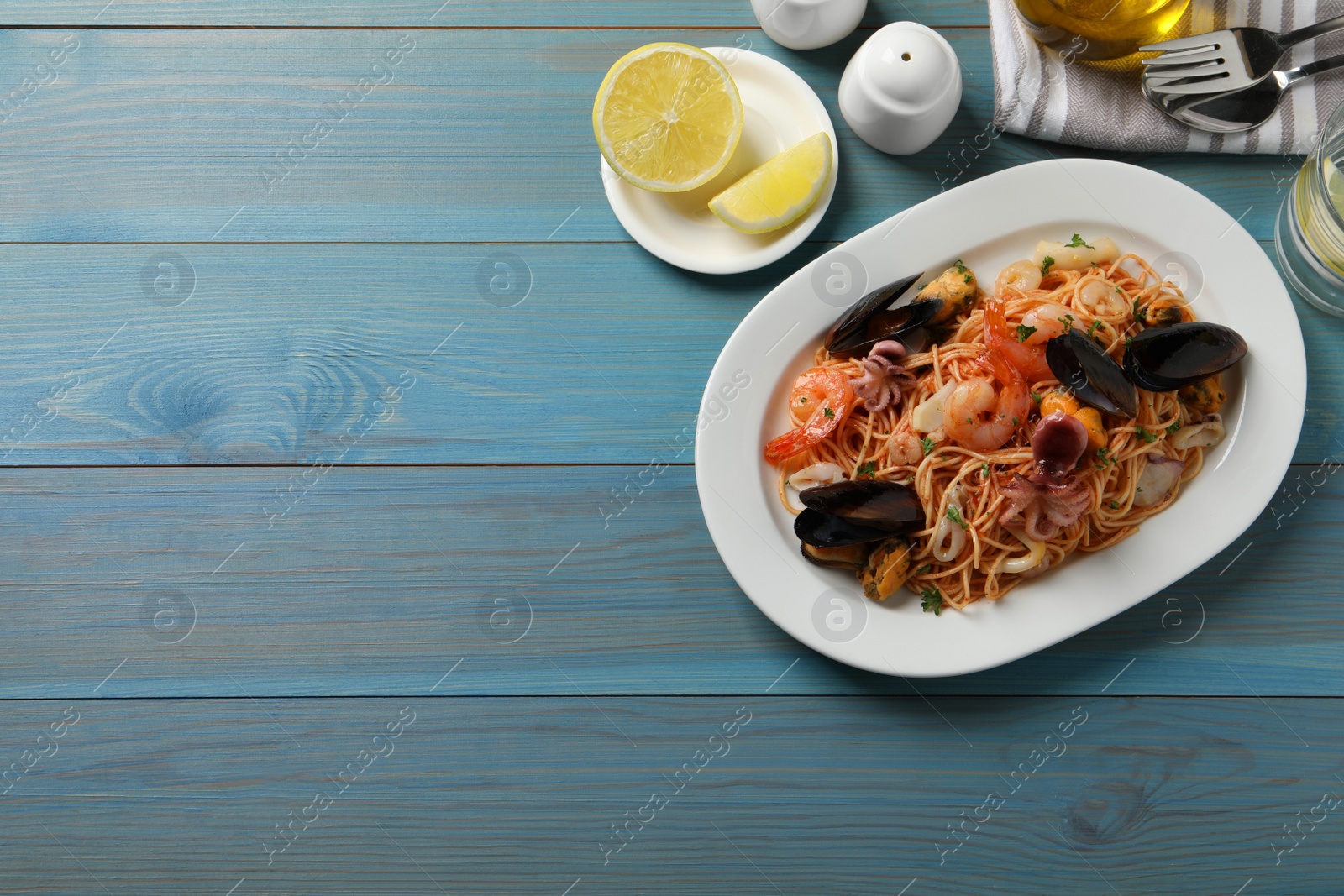 Photo of Delicious spaghetti with seafood served on turquoise wooden table, flat lay. Space for text