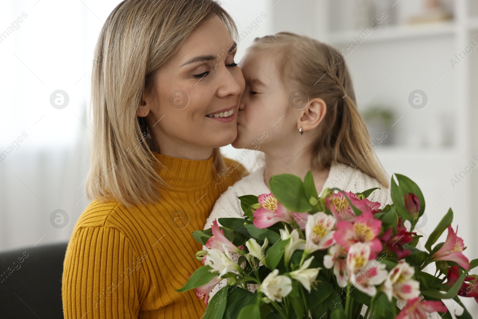 Photo of Little daughter kissing and congratulating her mom with bouquet of alstroemeria flowers at home. Happy Mother's Day