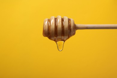 Photo of Pouring honey from dipper against yellow background, closeup. Space for text