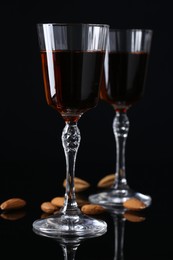 Liqueur glasses with tasty amaretto and almonds on black table, closeup