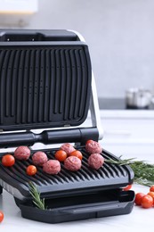 Electric grill with meatballs, tomatoes and rosemary on white table indoors