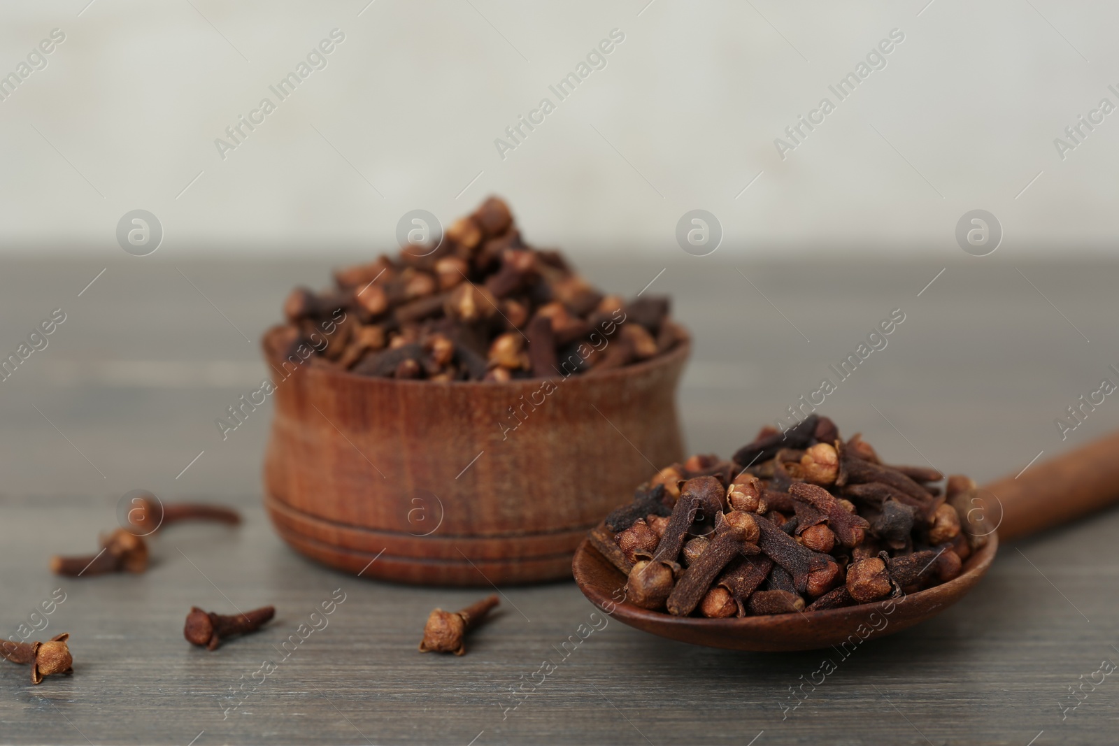 Photo of Spoon and bowl of aromatic dry cloves on wooden table