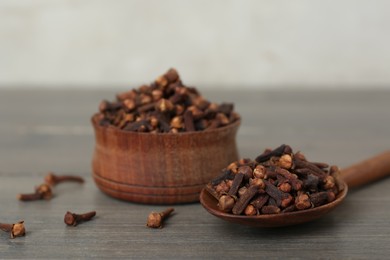 Spoon and bowl of aromatic dry cloves on wooden table