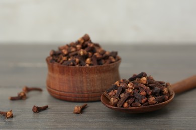 Photo of Spoon and bowl of aromatic dry cloves on wooden table