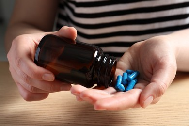 Photo of Woman pouring pills from bottle at wooden table, closeup